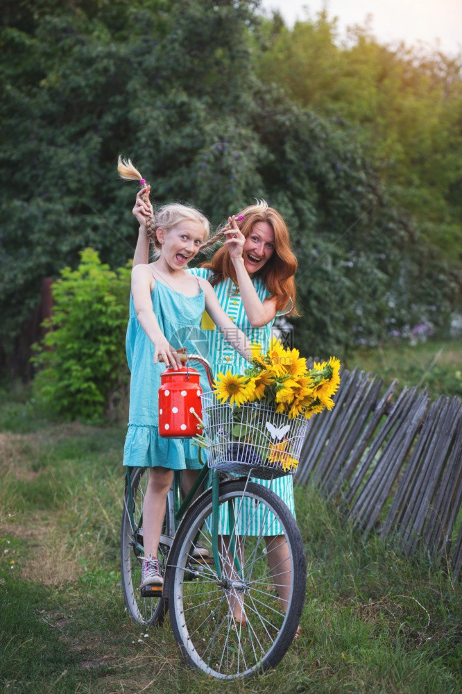 疯狂的快乐女孩骑着一辆旧自行车带着一篮子向日葵复古风格在村子里过暑假家庭母亲和女儿图片