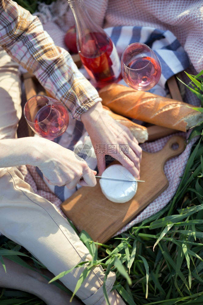 女孩在野餐篮子和面包葡萄酒眼镜旁切烤奶酪图片