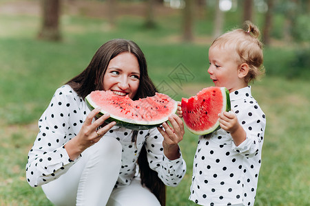 小朋友抱西瓜快乐的母亲和女儿在夏季公园吃西瓜快乐的笑脸家庭在公园吃西瓜母亲和女儿一起度过时间饮食维生素健康的食物概念选择焦点饮食健康的物概念背景