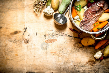 一大壶汤配有牛肉和新鲜蔬菜木制背景图片