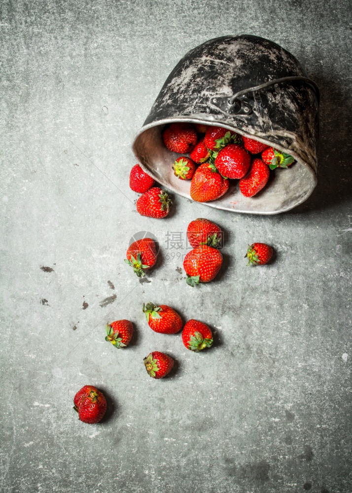 成熟的草莓在一块老锅里石头桌上图片