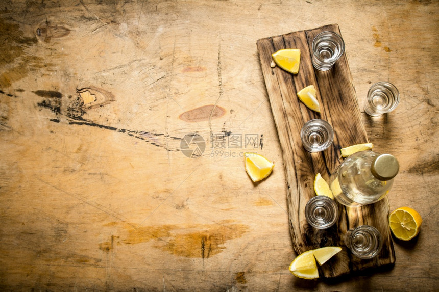 一瓶伏特加配有杯子和柠檬放在木质背景上图片