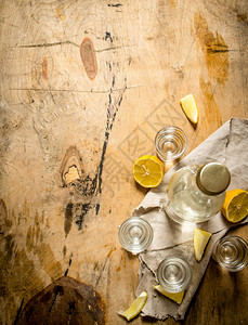 一瓶伏特加配有杯子和柠檬放在木质背景上图片