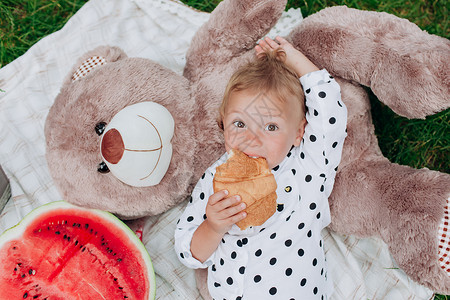 可爱的小女孩在野餐时躺毯子上吃羊角面图片