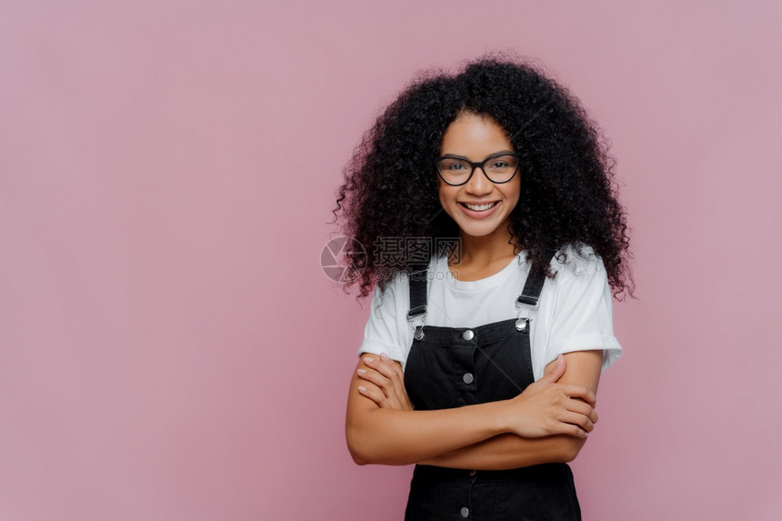 可爱的十几岁女孩美发照片折臂戴眼镜穿白色T恤衫和黑内衣看着很愉快的相机站在紫色背景上复制文本空间图片