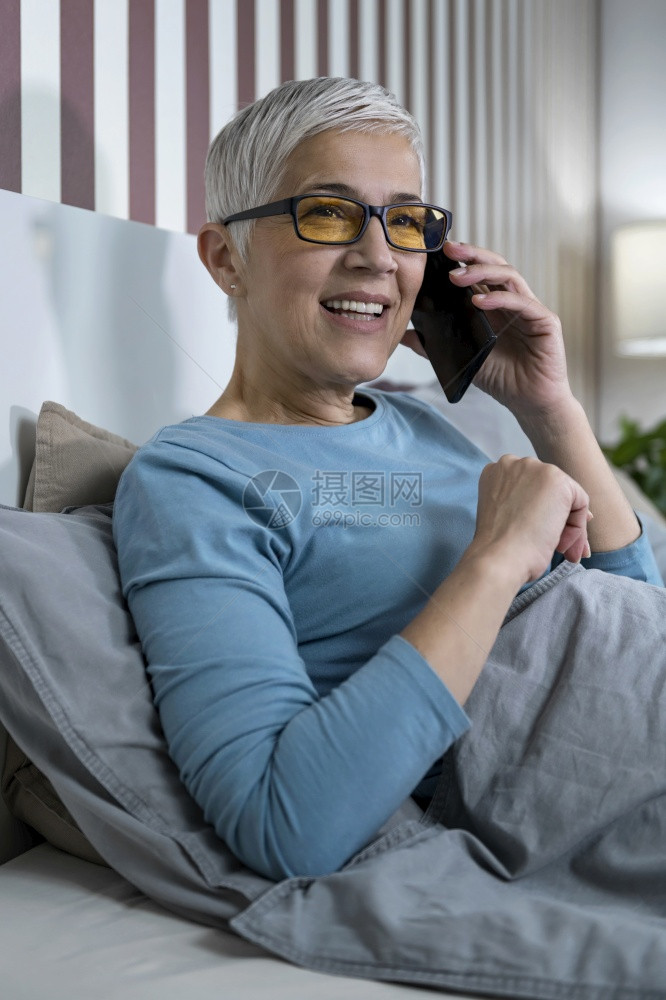 红灯挡住眼镜成年女人在睡觉前家通过电话聊天在睡觉前家休息蓝灯挡住眼镜成年女人通过电话交谈图片