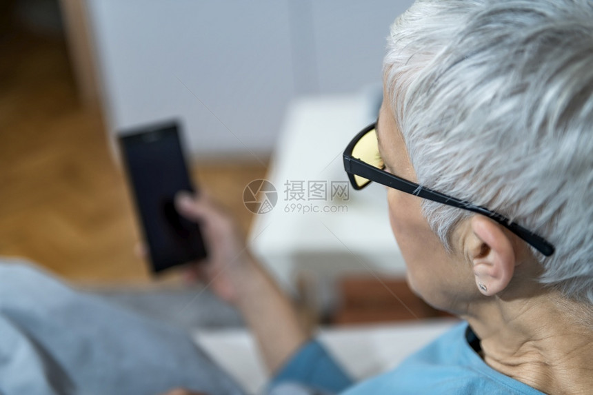 成年妇女躺在床上手持智能电话成年妇女晚上用蓝灯挡住眼镜以尽量减少对睡眠的干扰图片