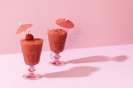 两杯草莓冰淇淋子里有鸡尾酒伞粉红背景严酷的光线夏天美味的假尾巴健康饮食料背景图片