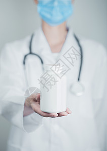 戴蓝色面罩的医生以疗面罩持有灰色医院墙底的塑料药箱抗生素维他命和治疗药片背景图片