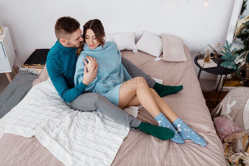 家庭圣诞节日爱和人的概念家庭爱和人的概念家庭床上穿着蓝色毛衣的幸福夫妇家庭床上穿着蓝色毛衣的快乐时装夫妇图片