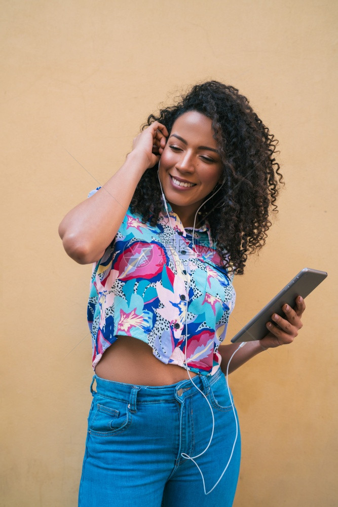 年轻快乐的美国拉丁女人肖像在她数字平板电脑技术概念上聆听音乐图片