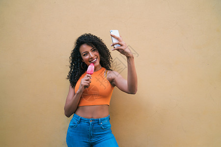 在吃冰淇淋时用手机自拍的for妇女肖像技术和生活方式概念背景