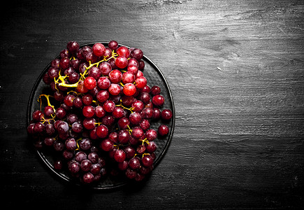 红色葡萄枝在盘子上黑色木头背景图片