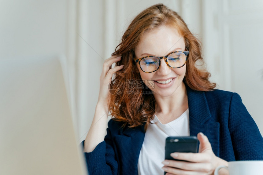 满意的红发女使用现代电子设备检查新闻在线通信和搜索息坐在工作场地使用高速互联网连接图片