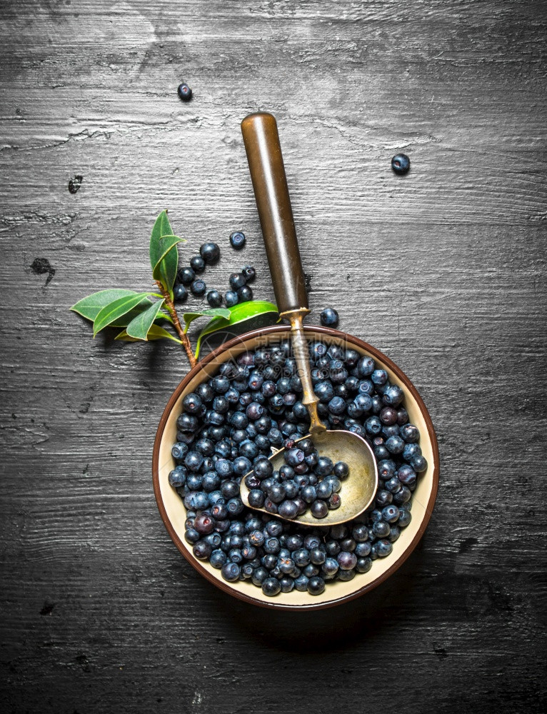 蓝莓和勺子放在杯里黑木背景图片
