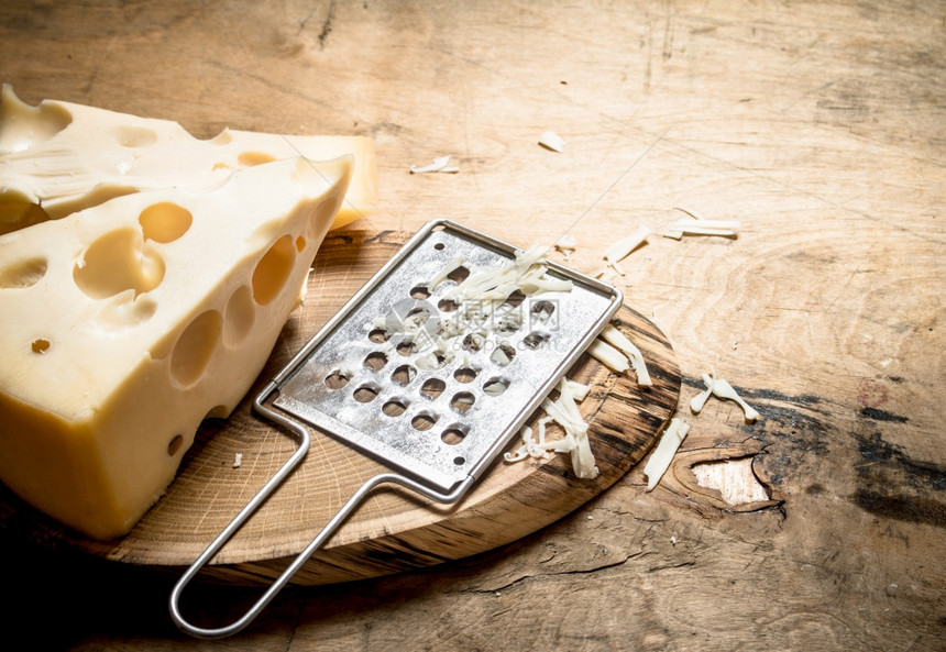 一块奶酪和板上的磨刀放在木制桌子上图片