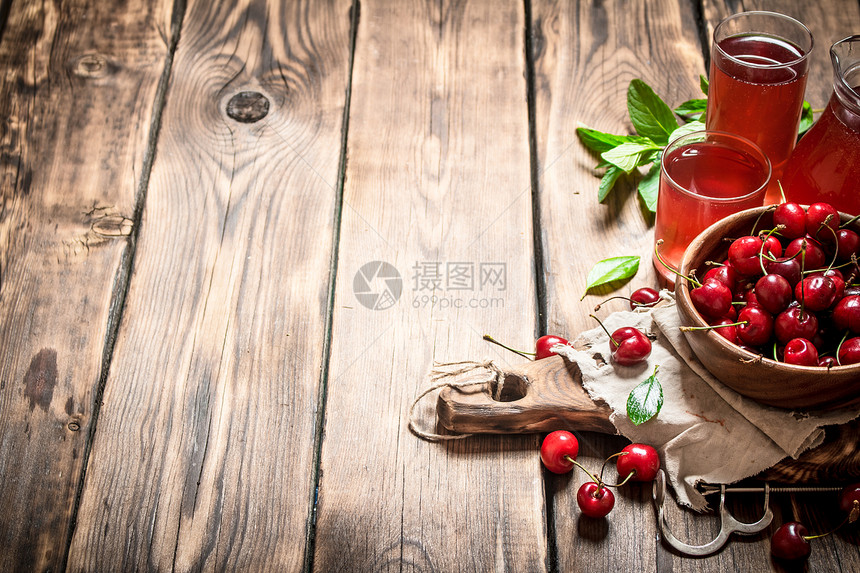 新鲜樱桃和杯子里的果汁木质背景图片