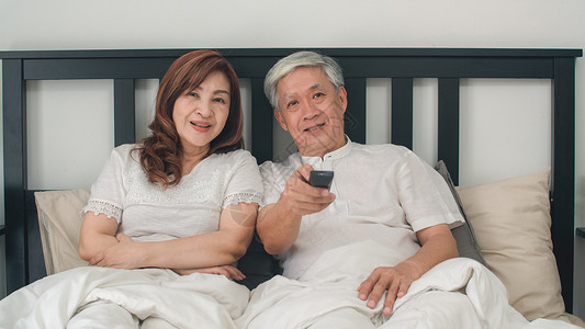 asi夫妇在家卧室看电视在家里放松时躺床上享受爱的时刻图片