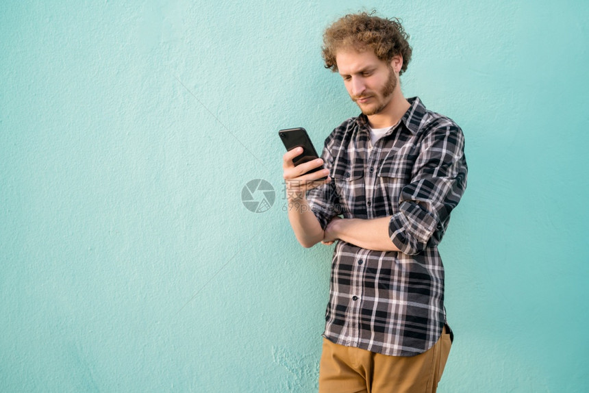 年轻人在蓝色背景下使用手机的肖像图片