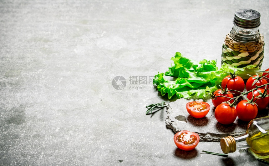 有生菜和橄榄油的新鲜西红柿在石头背景上图片