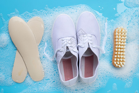 装有粉末洗涤水溶解泡沫的运动鞋和蓝底的木刷子洗脏鞋背景图片
