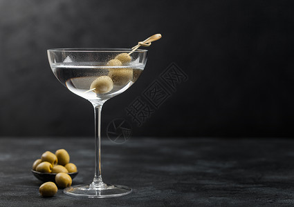 伏特加马提尼酒鸡尾在现代玻璃杯里橄榄在金属碗里竹棍在黑色背景上背景