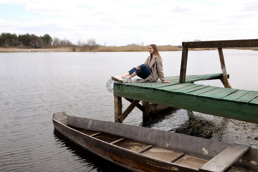 年轻美女在春天坐河边的木桥上海岸附近的老船有选择聚焦点有选择聚焦点图片