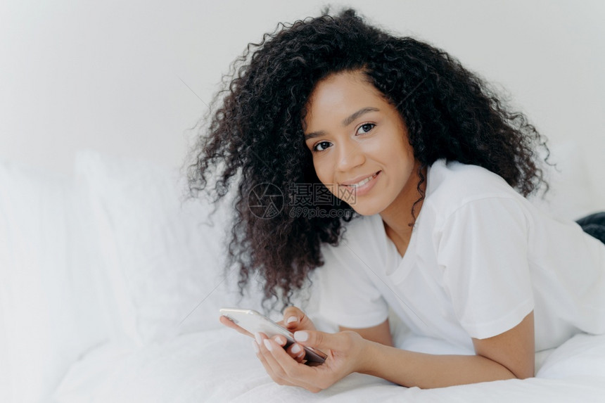 穿着T恤衫现代技术放松在卧室里摆姿势阅读短信使用免费互联网图片