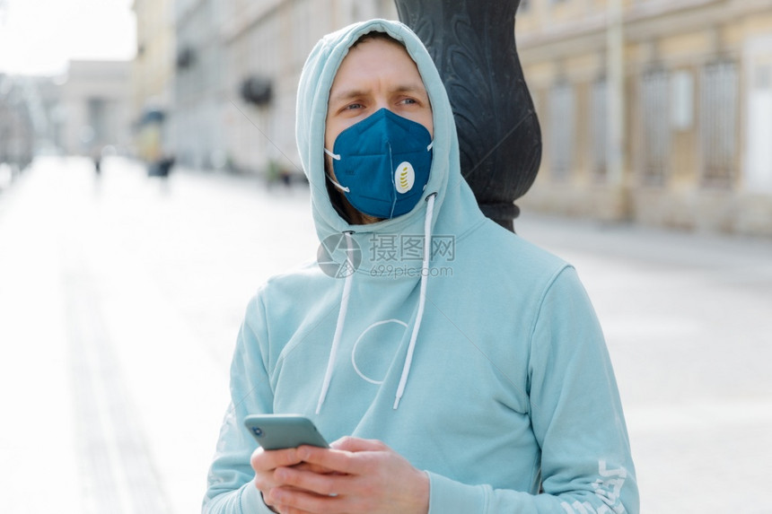 年轻人在户外横向拍摄的青年男子身戴呼吸器面具以保护健康用手机在街上行走冠状爆发时保护自己在网上跟踪新闻穿着连帽衫图片