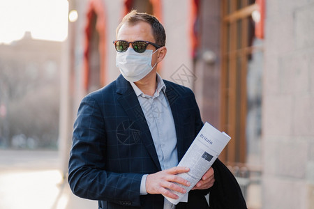 商人戴防传染病的保护面罩阅读报纸穿着优雅在户外布置思考如何防止的新冠状背景图片
