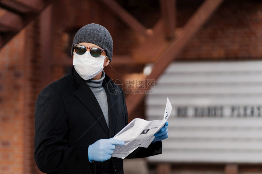 在冠状流行期间人横向开使用预防措施戴面罩和橡胶手套阅读报纸图片