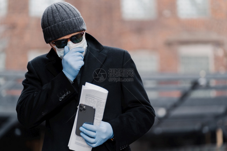在户外拍摄的人咳嗽试图不传播冠状感染戴防护面具和手套持有报纸和手机呼吸问题保护图片