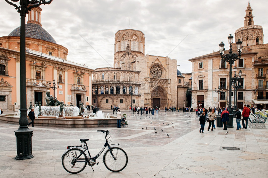 201年8月3日ValenciSpnfuetdluria喷泉自行车和游客在ValenciCthedrl广场有教堂和钟楼背景图片