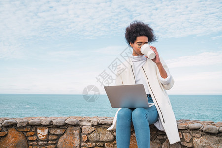 使用笔记本电脑坐在海洋边喝杯咖啡科技概念图片