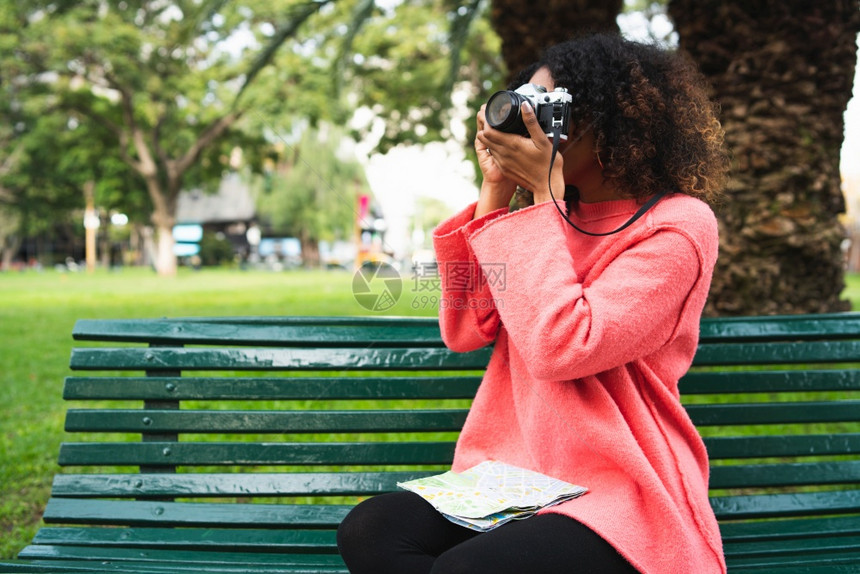 年轻美籍女子在公园里持有时使用专业相机图片