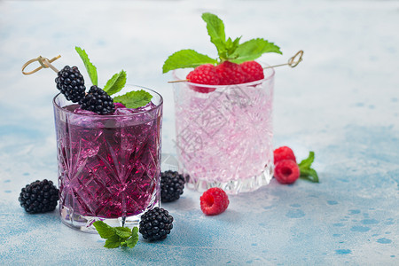 杯装果汁夏季鸡尾酒用黑莓和粉红色柠檬汁装在晶杯中用冰块和薄荷装在浅蓝色背景上苏打汽水和酒精混合背景
