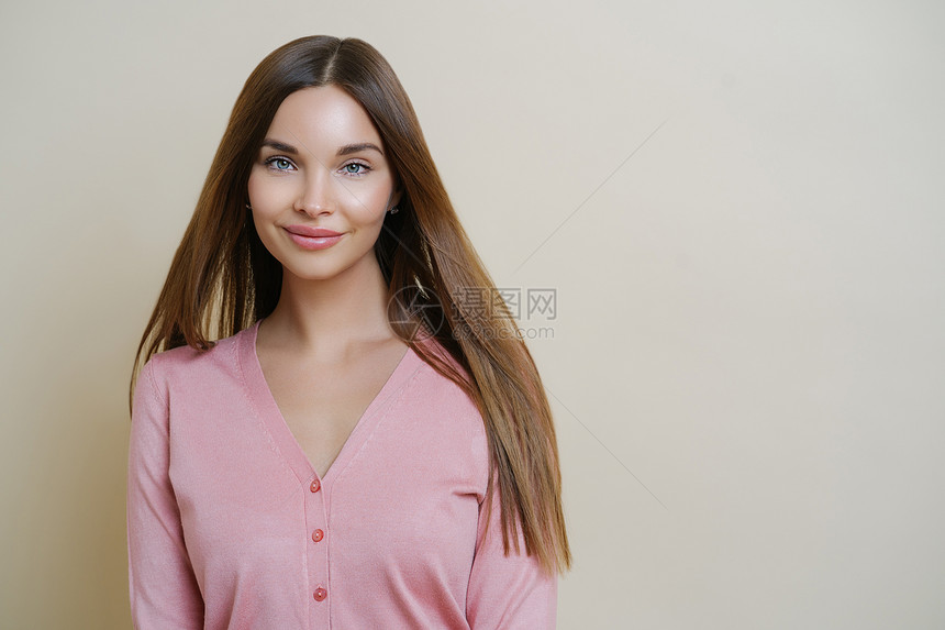 迷人的欧洲女横向肖像轻地对着镜头微笑长的直发穿着小毛衣要去户外散步站在蜜蜂工作室的背景上图片