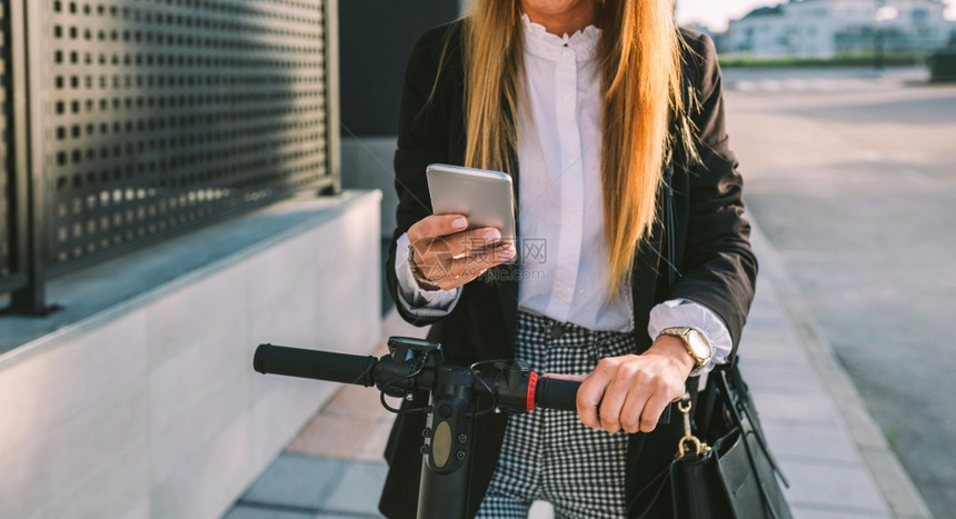 在街上用电子摩托车看手机的女商人图片