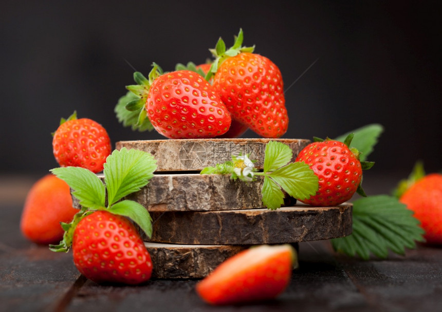 有机新鲜生草莓在深色背景的木材圆板上放叶子最好的夏季浆果图片