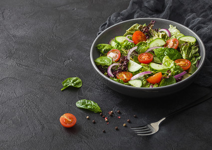 新鲜蔬菜沙拉配有生和西红柿洋葱和黑碗菠菜底配有餐叉和厨房布图片