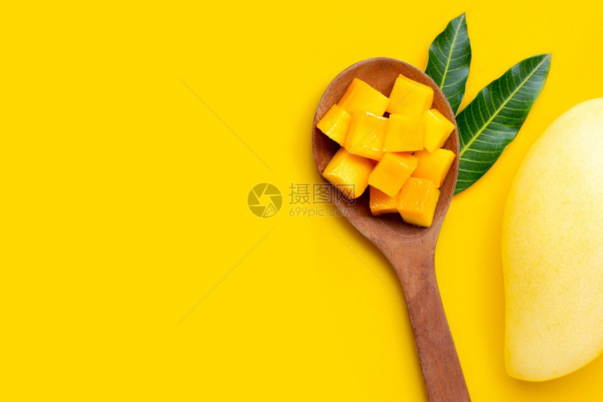 在黄色背景的木勺上切成熟芒果立方块复制空间图片