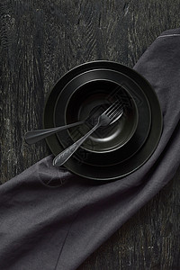 由陶瓷板上的黑颜色制成配有勺子和叉的黑颜色用同样的石本背景提供纺织毛巾或餐复制空间由黑色用具陶瓷板勺子叉和纺织品餐巾提供的厨房桌背景图片