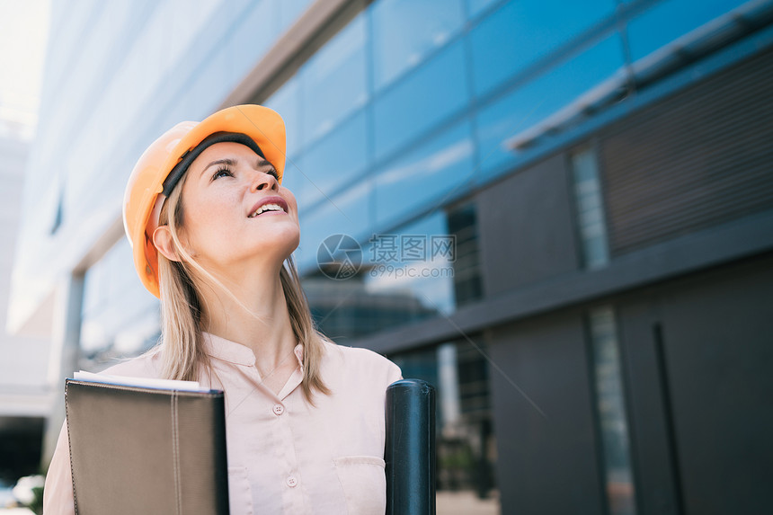 女专业建筑师身着黄头盔的肖像并观看现代建筑室外工程师和概念图片