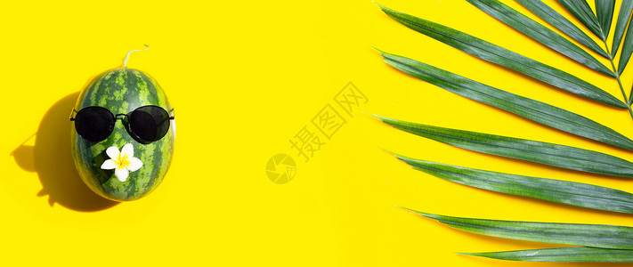 暴龙太阳镜黄底带太阳眼镜和热棕榈叶的西瓜享受暑假的概念背景