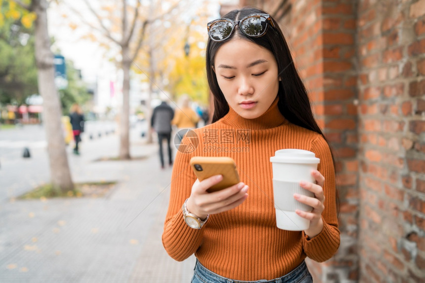 年轻女使用手机在街上端咖啡时图片