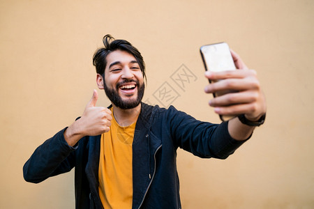 嗜酒具有吸引力的年轻人用摩菲利手机和黄色墙对着拍自的肖像技术概念背景