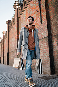 扛着袋子男人年轻英俊男子在街上散步时拿着购物袋的肖像城市商店概念背景