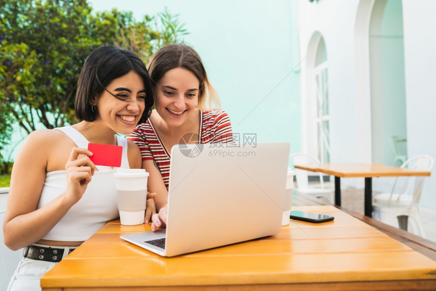 两位年轻朋友在咖啡店用笔记本电脑和信用卡在线购物的肖像图片