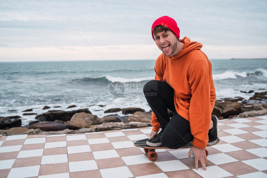 年轻人的肖像与他滑板玩得开心并练习他的把戏在背景海洋图片