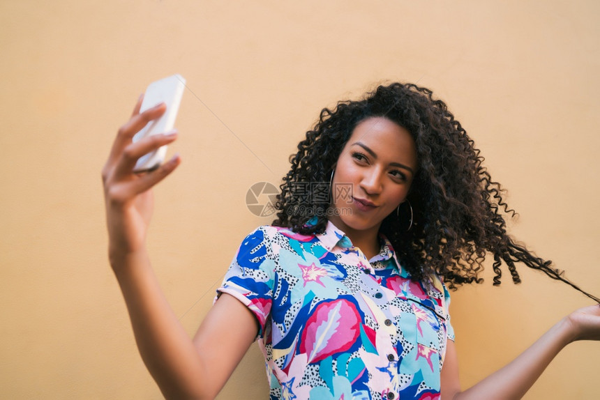 年轻for女人用手机自拍与黄色墙对着技术概念图片